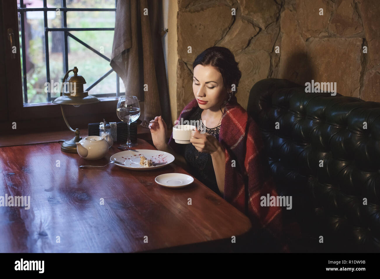 Femme boit du thé dans un café le soir, elle mange le gâteau. Banque D'Images