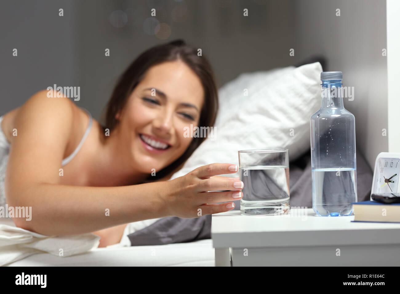 Heureux fille assoiffée d'attraper un verre d'eau sur le lit dans la nuit à la maison Banque D'Images