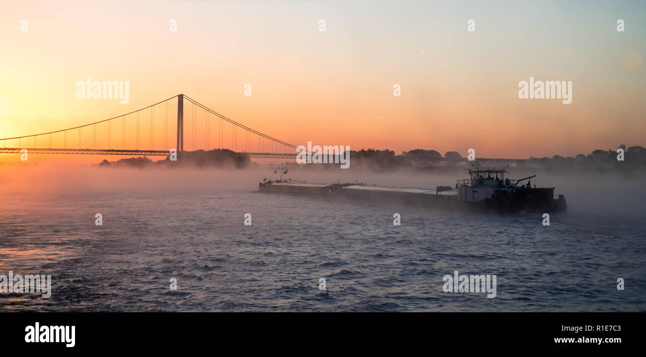 Misty morning sunrise sur un pont suspendu avec commercial river péniche sur le Rhin Banque D'Images