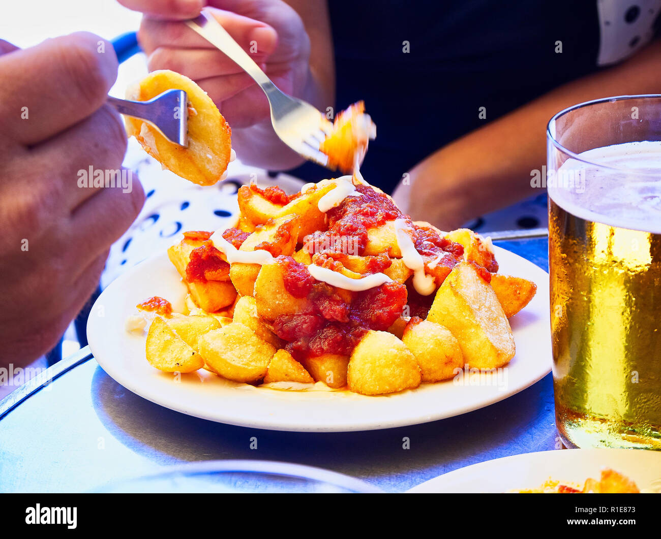 Les gens de goût une partie de patatas bravas sur une table métallique. Frites garnies de sauce épicée, l'un des plus communs des tapas espagnoles. Banque D'Images