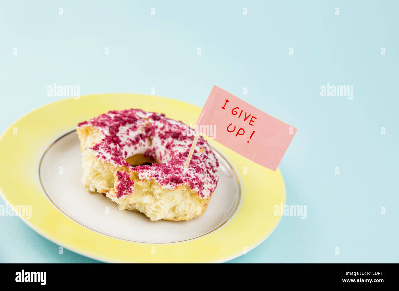 À moitié mangé donut avec glaçage rose et blanc sur plaque jaune avec remise d'un drapeau texte : J'abandonne, sur fond bleu. Studio shot conceptuel de nous Banque D'Images