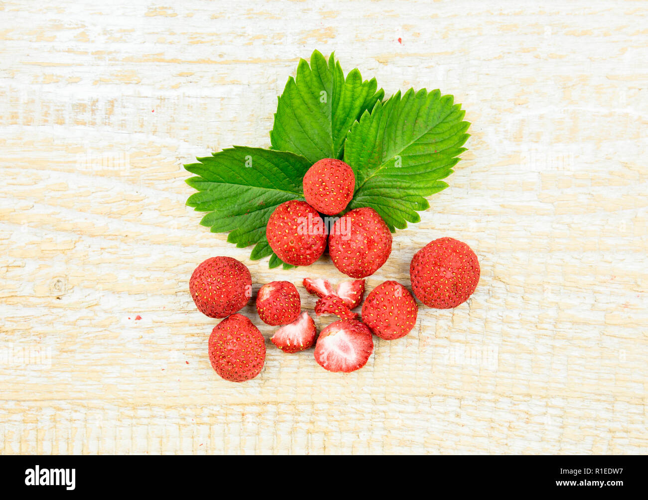 Ensemble de lyophilisé et morceaux de fraises sur le vert des feuilles de fraisier, collation santé pleine de vitamines et de la nutrition sur fond de bois naturel. Banque D'Images