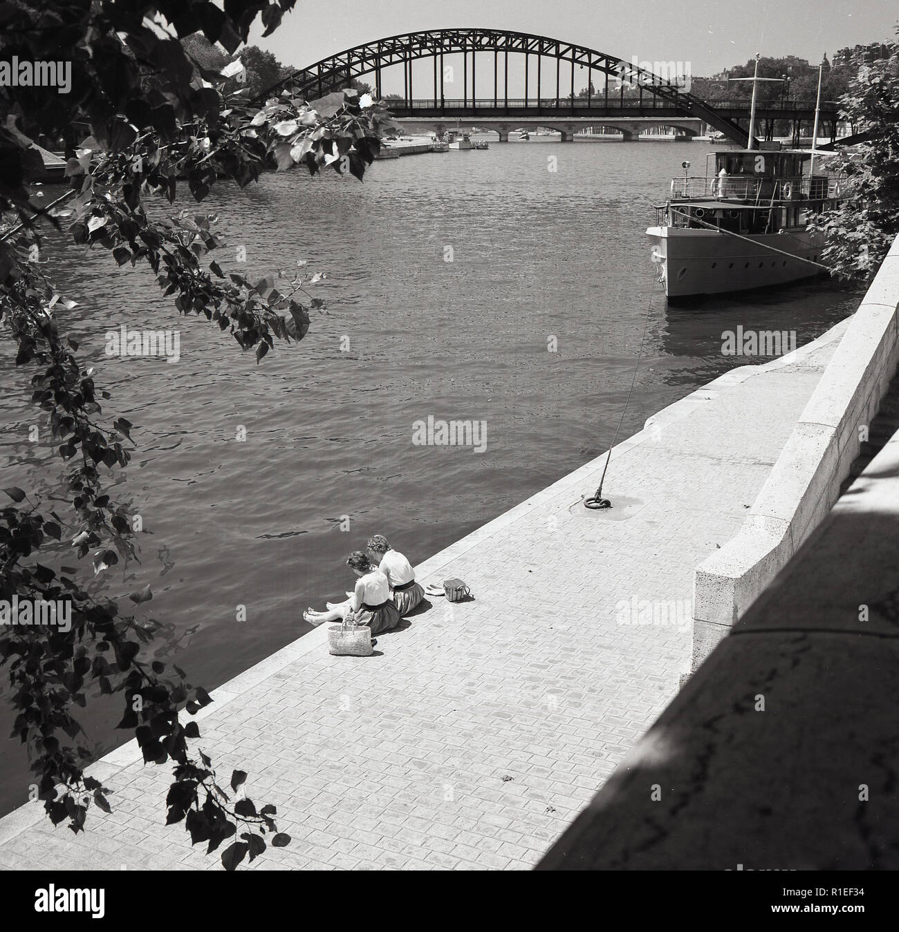 Années 1950, historiques, deux jeunes femmes assis à côté de la rivière sur une passerelle par la Seine, Paris, France. Banque D'Images
