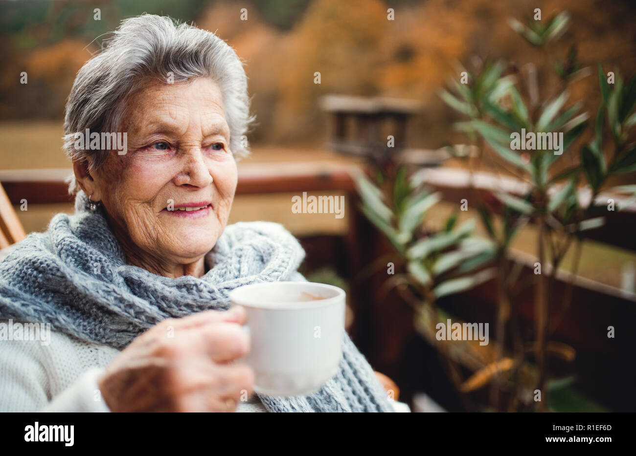 Une vieille femme debout à l'extérieur sur une terrasse sur une journée ensoleillée à l'automne. Banque D'Images