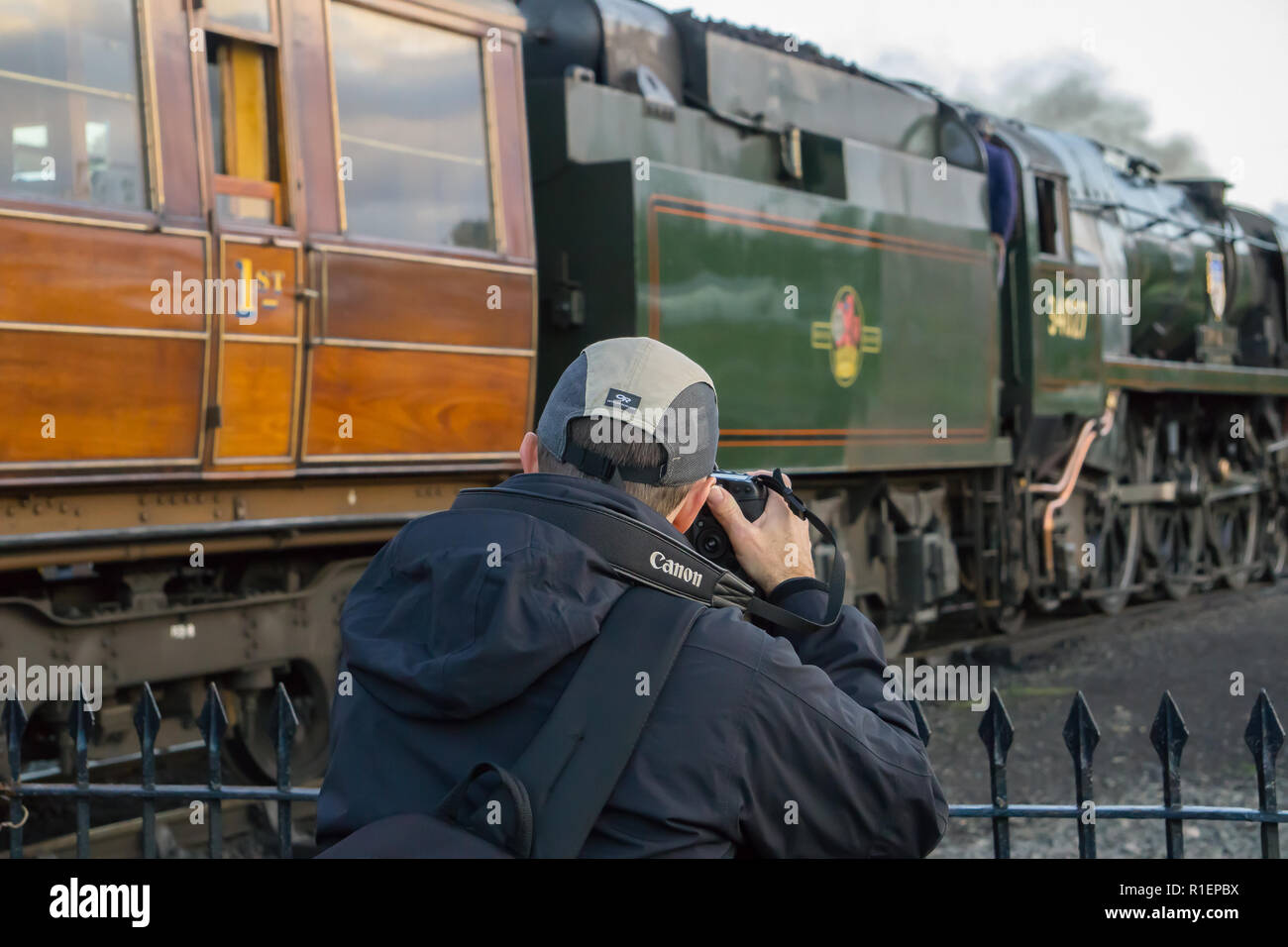 Close up mâle isolé photographe, vue arrière, prendre des photos de vintage UK train à vapeur et voitures en attente de départ, gare ferroviaire patrimoniale. Banque D'Images