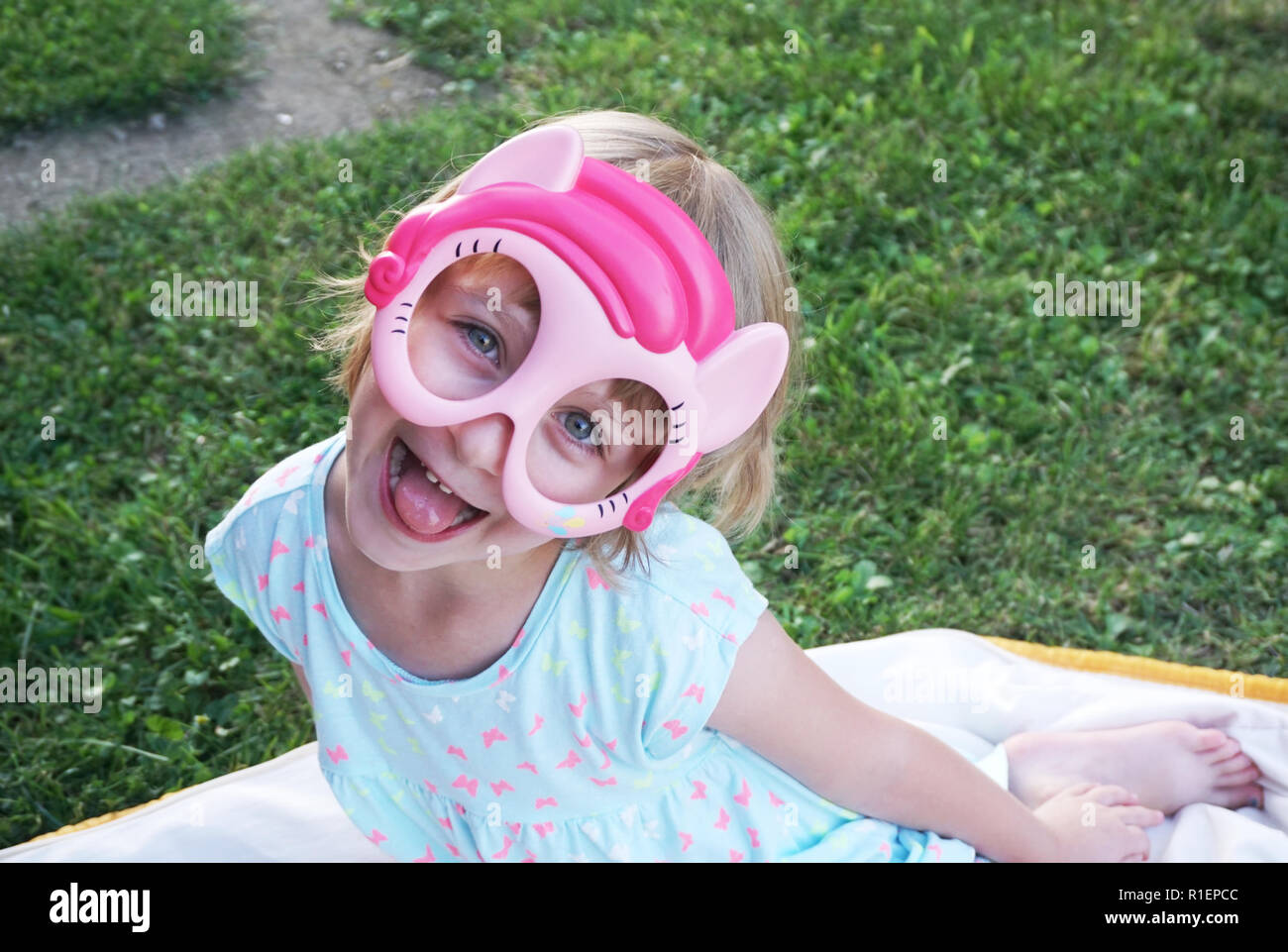 Heureux adorable petite fille faire drôle de visage avec masque sur elle et à la recherche dans l'appareil photo Banque D'Images