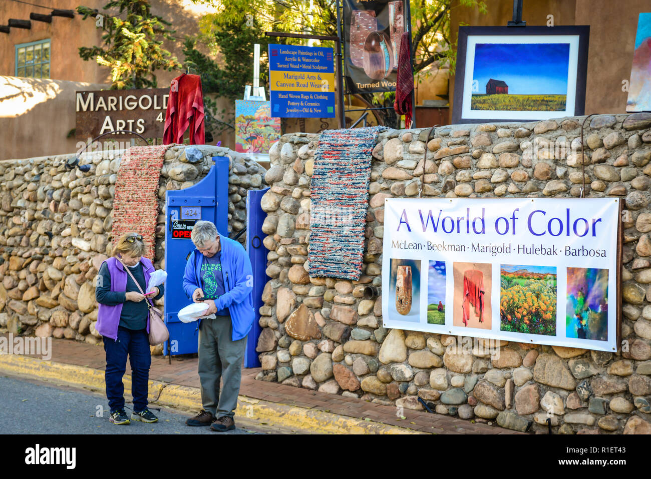 Vieux couple contrôler leur téléphone sur les lieux historiques de Canyon Road à Santa Fe, NM, entouré de galeries d'art et l'architecture historique de charme Banque D'Images