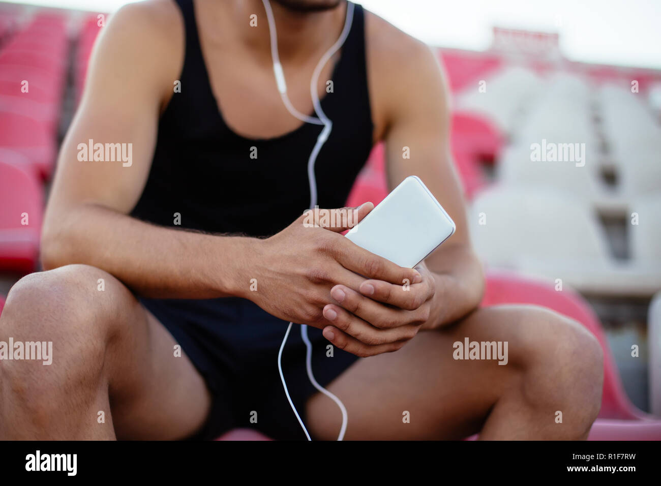 Sportsman listening music assis sur les sièges du stade, se détendre après l'entraînement. L'accent sur le smartphone. Banque D'Images