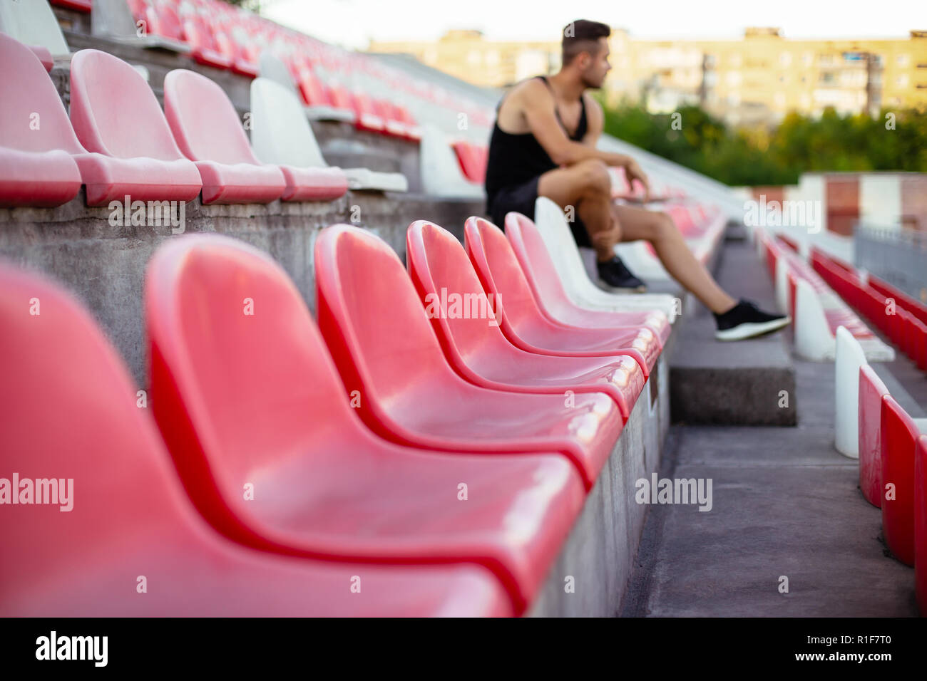 Des rangées de sièges vides dans un stade sportif, jeune sportif sur l'arrière-plan. Des chaises en plastique rouge et blanc pour les fans d'attente Banque D'Images