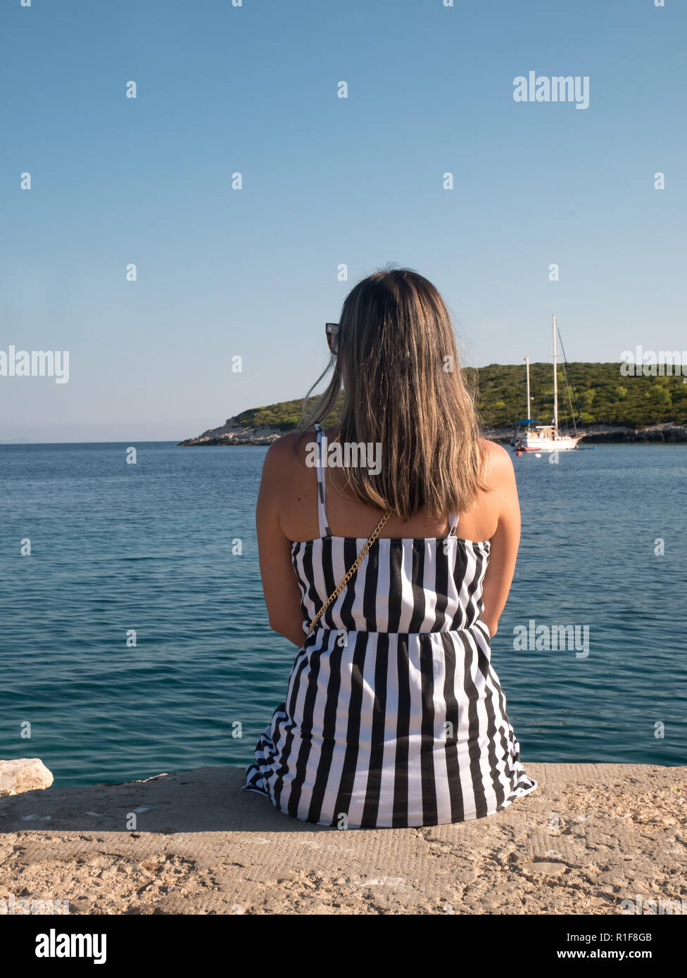 Jeune femme en robe noir et blanc assis par le calme mer Adriatique Banque D'Images