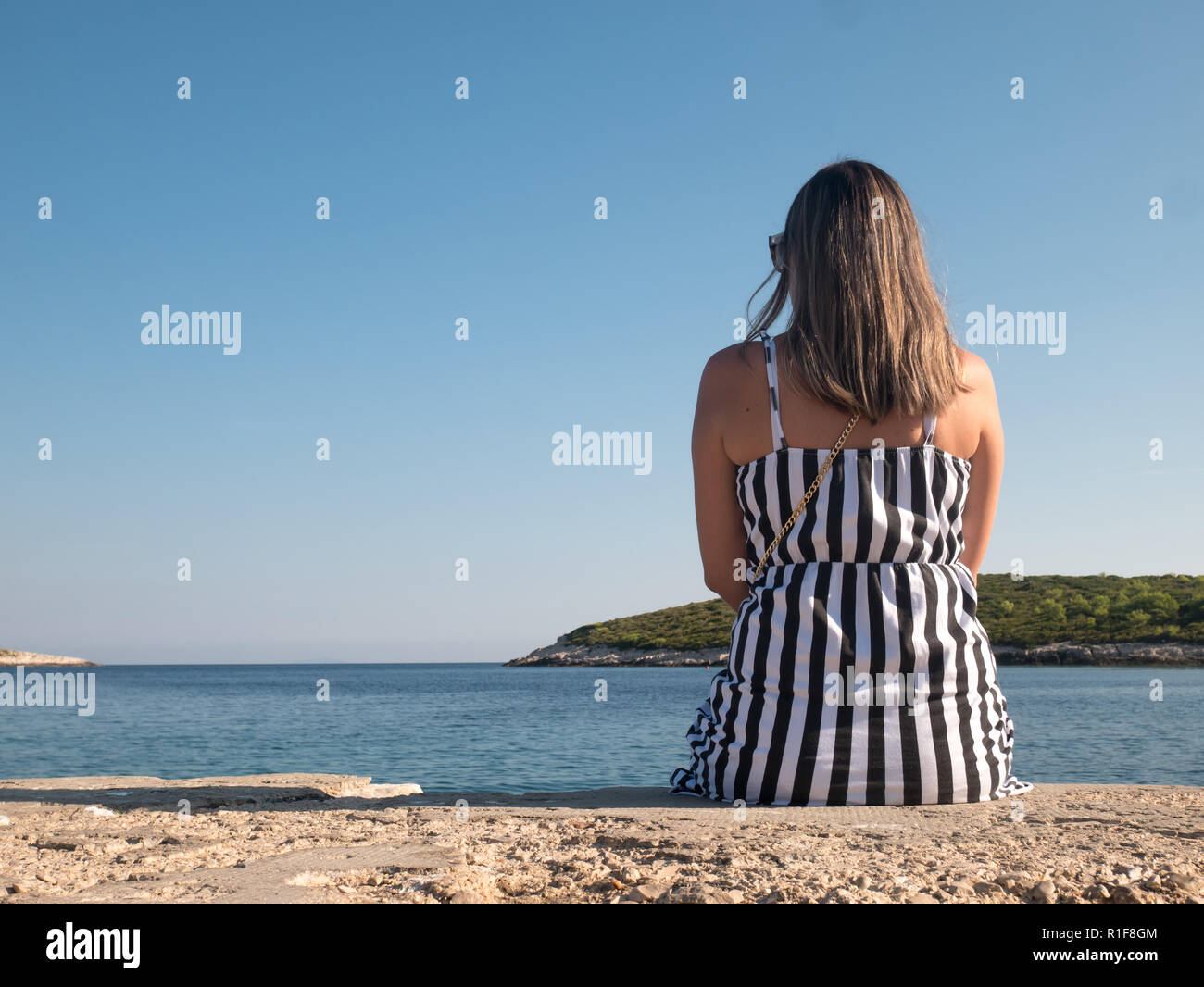 Jeune femme assise seule sur un quai de pierre par le bleu de la mer sur la côte Adriatique Banque D'Images