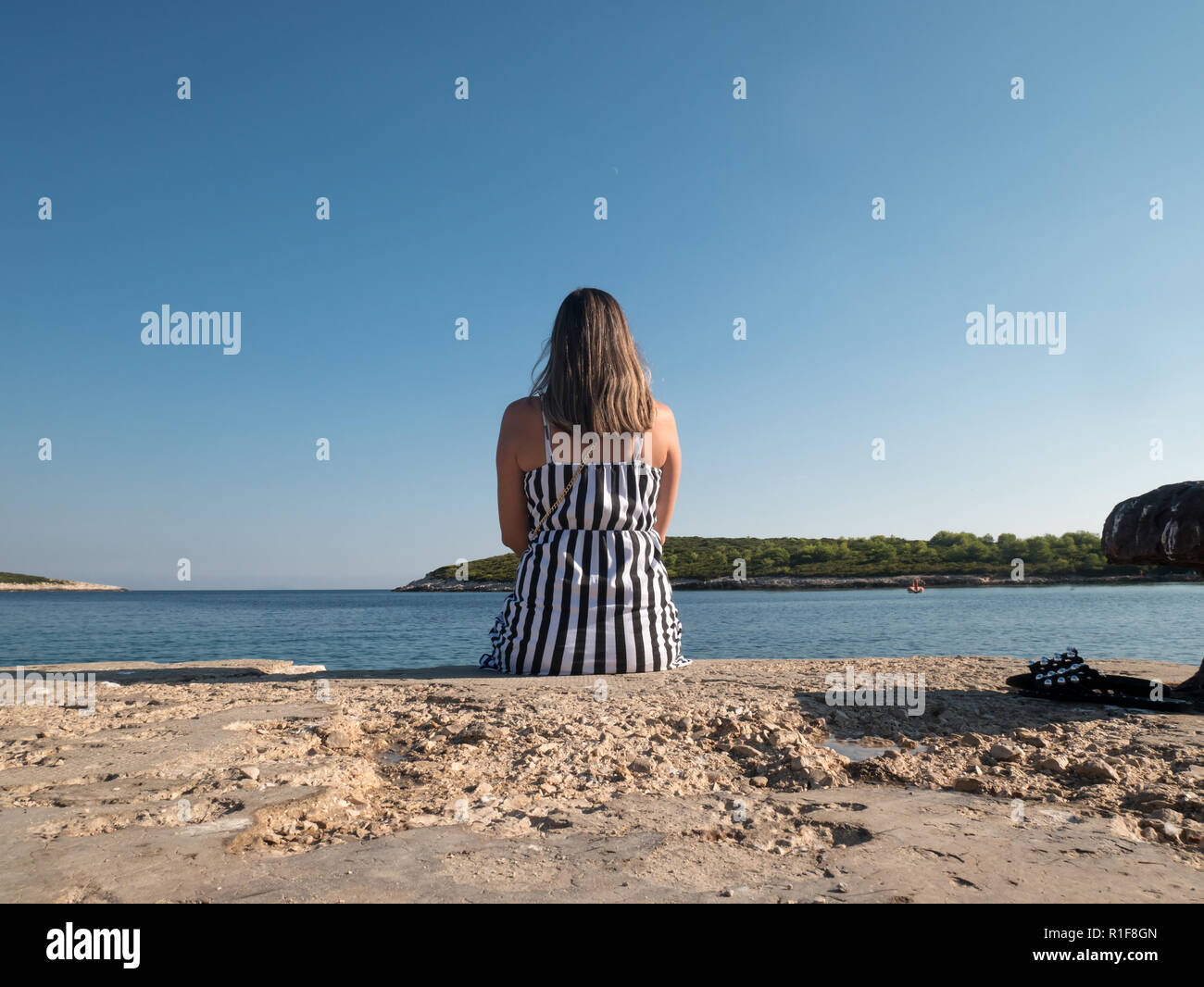 Young caucasian woman sitting on dock en pierre près de la mer de l'arrière Banque D'Images