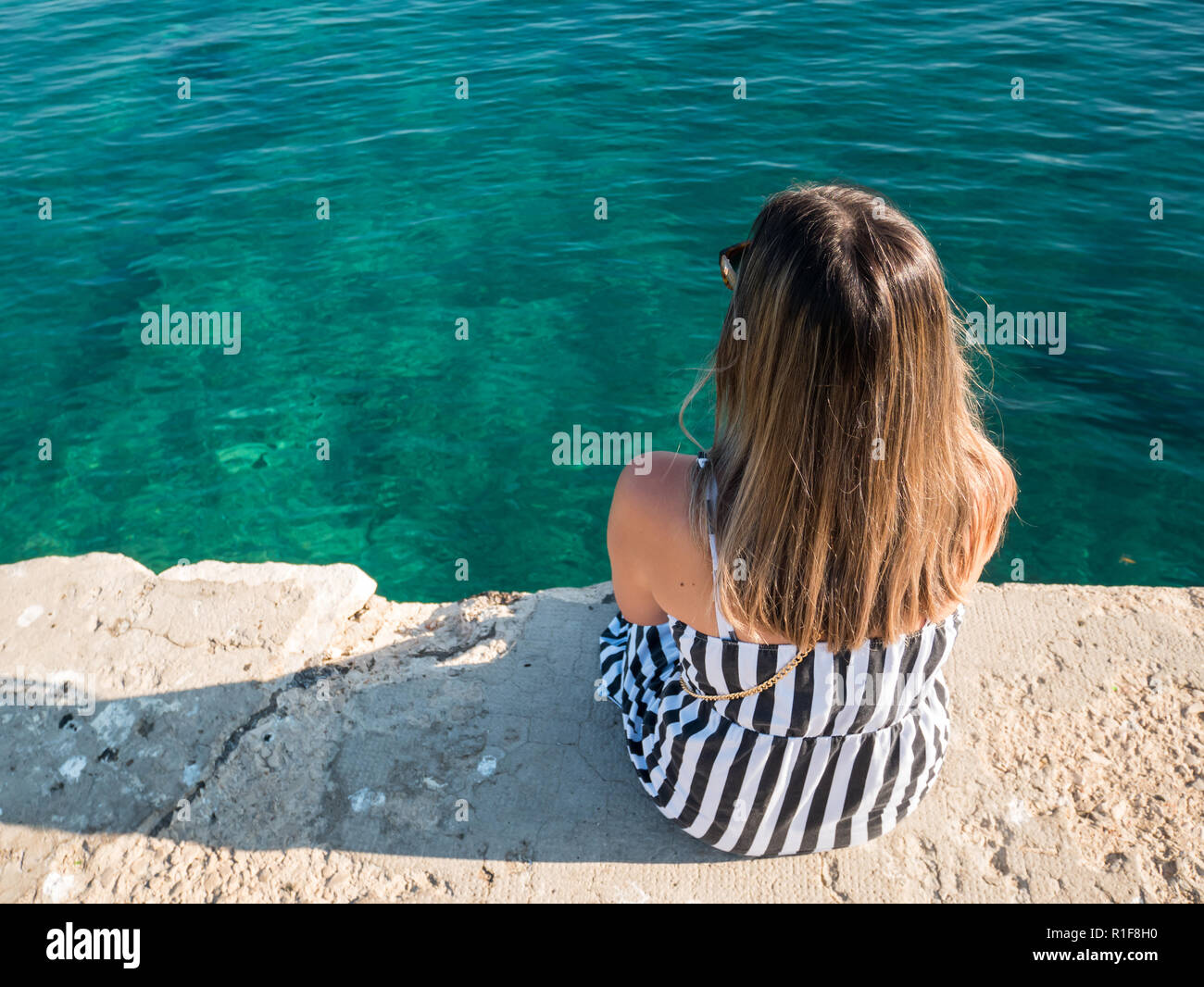 Jeune femme assise sur un quai en pierre et à la recherche en mer Banque D'Images