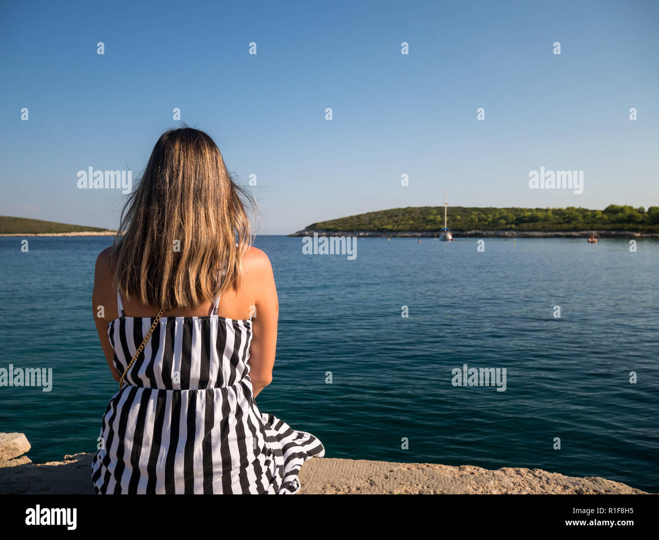 Jeune femme avec de beaux cheveux assis sur un quai en pierre près de la mer sur l'île de Vis en Croatie Banque D'Images