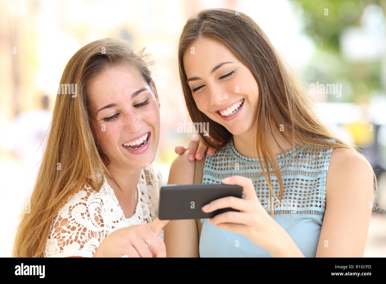 Deux amis heureux regardant des médias sur un smartphone horizontale dans la rue Banque D'Images