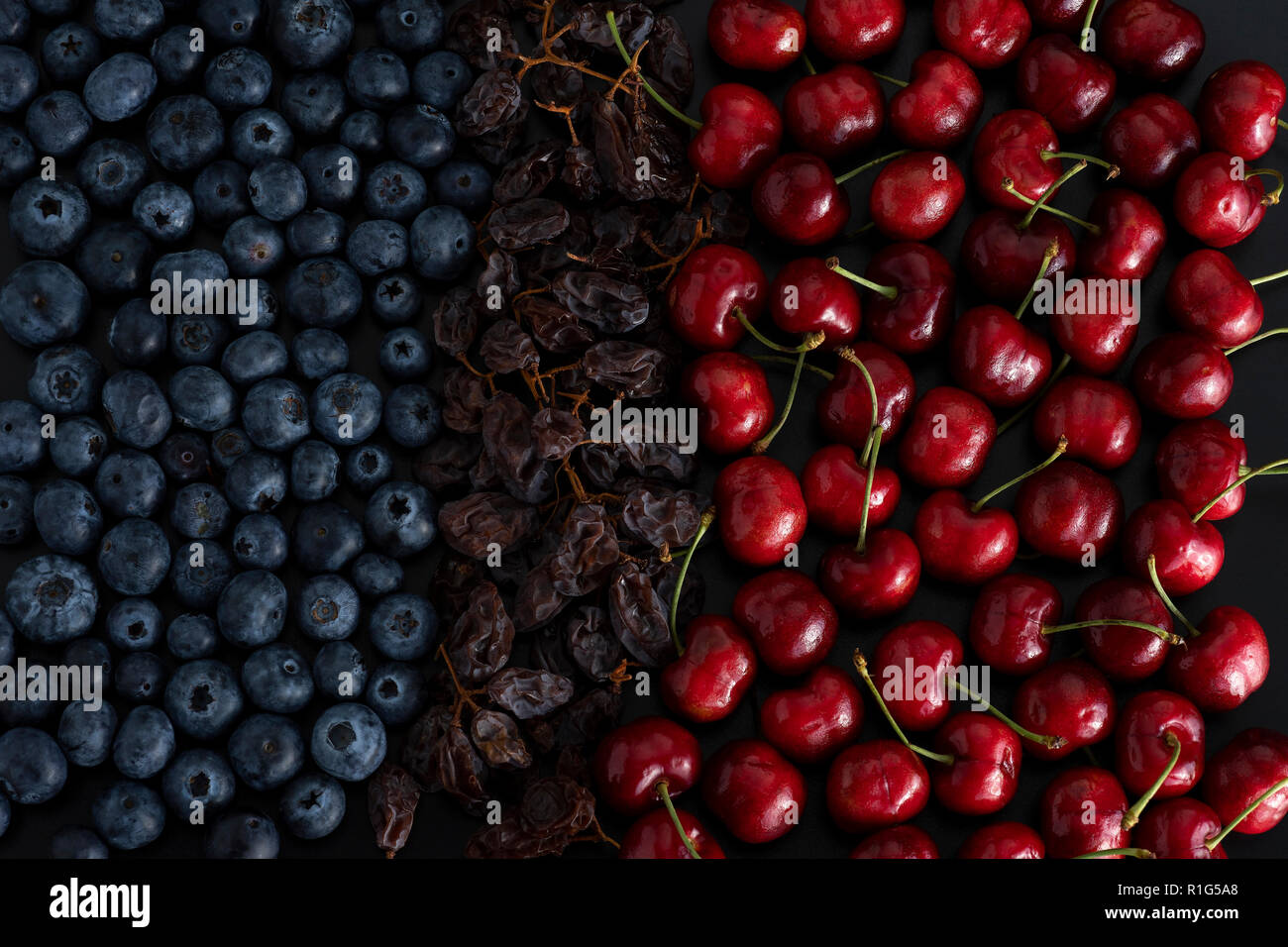 Bouquet de petits fruits bleu, séchés raisins et cerises isolé sur fond noir Banque D'Images