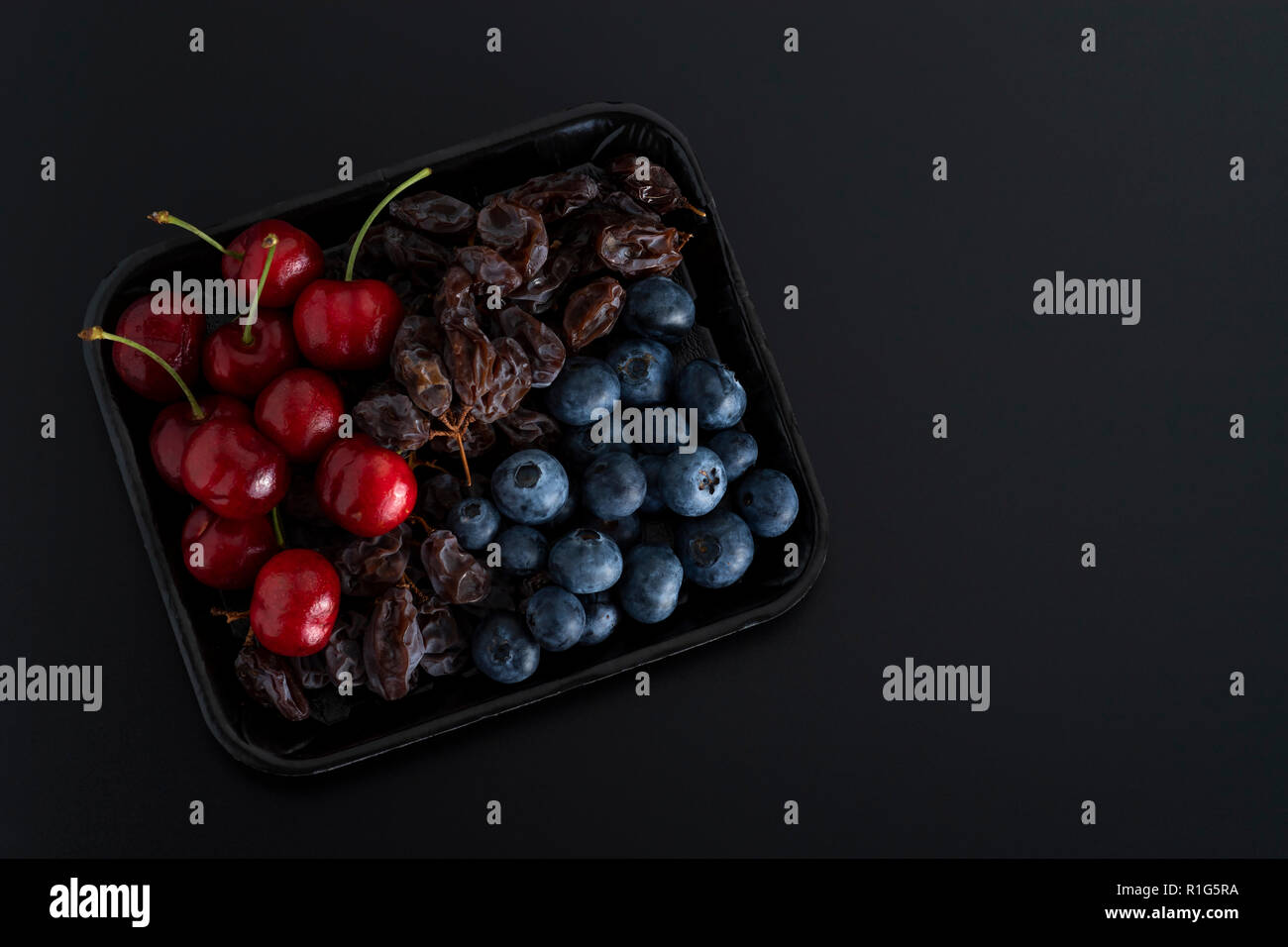 Tas de raisins secs, de petits fruits et de cerise bleu sur un plateau isolé sur fond noir Banque D'Images