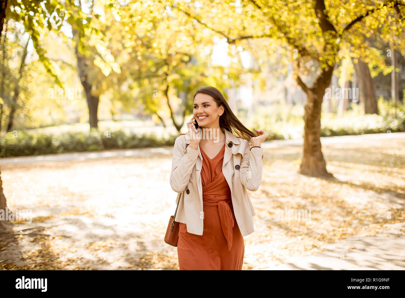 Happy young woman using cell phone in autumn park sur belle journée Banque D'Images