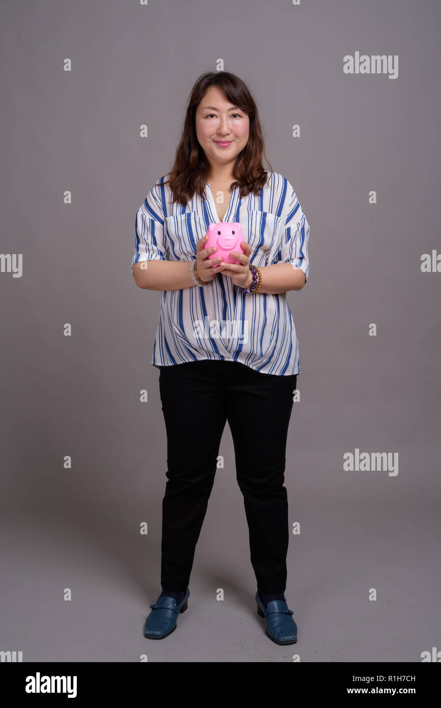 Portrait of mature japonais businesswoman holding piggy bank Banque D'Images