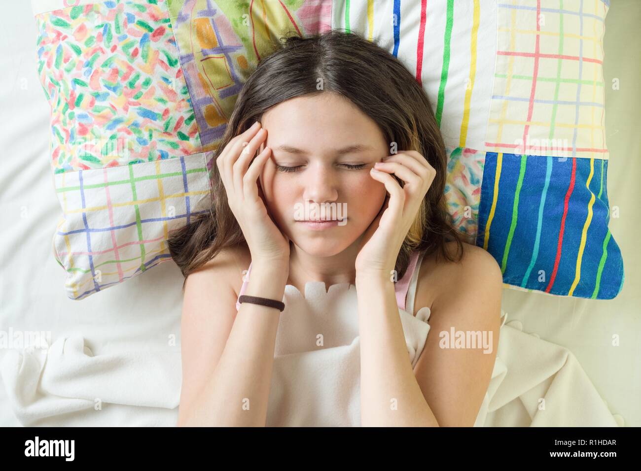 Face Close-up of teenage girl on oreiller avec les yeux fermé holding head avec les mains. Banque D'Images