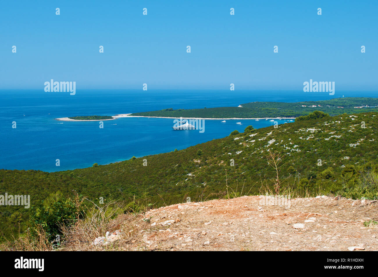 Un navire et plusieurs yachts dans la mer bleu azur dans une baie près de la côte d'une île avec des collines couvertes de vert forêt verdoyante. Le bleu ciel sans nuages. Banque D'Images