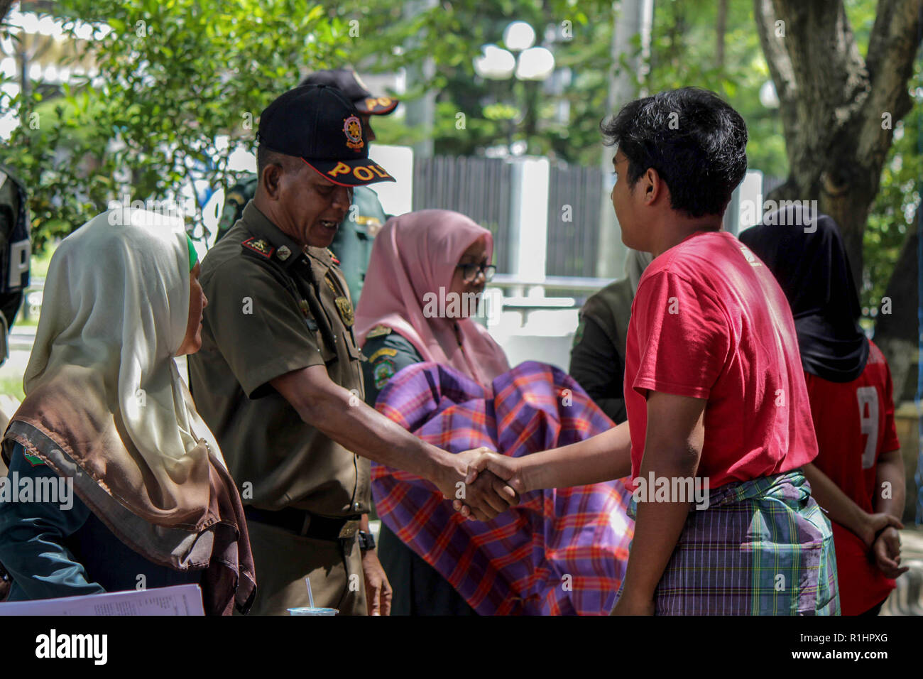 Agent de la Police de la charia islamique (Wilayatul Hisbah) vu serrant la main d'un homme portant un sarong au cours de la routine des raids dans la ville de Lhokseumawe. Les agents de la Police de la charia islamique (Wilayatul Hisbah) fournir des sarongs pour ceux qui violent la loi de la charia islamique par la force dans la ville de Lhokseumawe, Aceh est la seule province de l'Indonésie qui a la plus grande population de musulmans dans le monde, qui met en œuvre la charia islamique comme la commission de la bastonnade et mener des raids de routine pour ceux qui sont bien habillés pour femmes et des shorts pour hommes. Banque D'Images