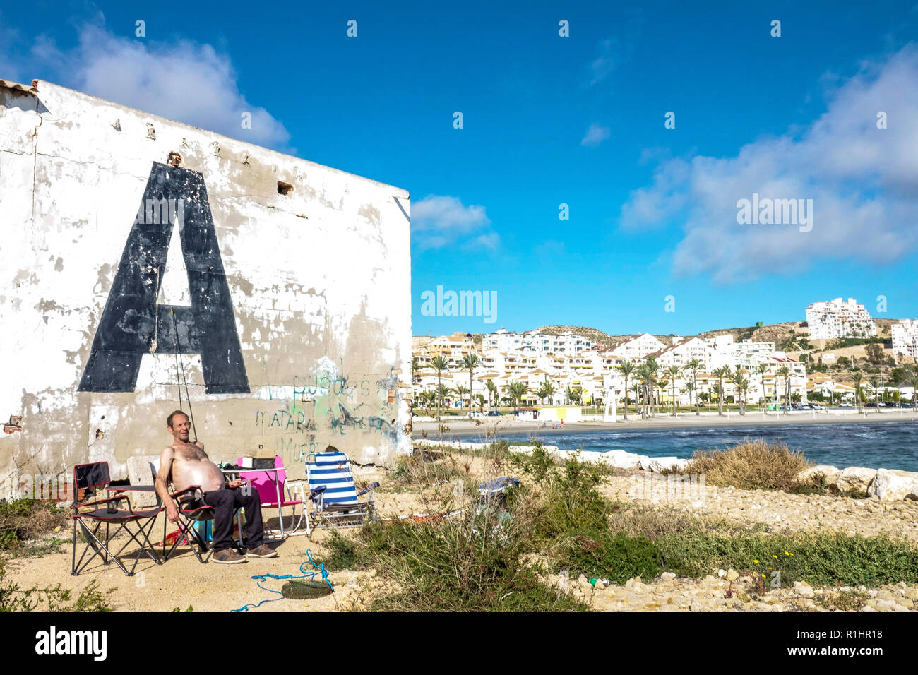 Plage à Santa Pola Espagne, un pêcheur senior relaxant sur la jetée en novembre, mural grande lettre Un énorme adulte senior Banque D'Images
