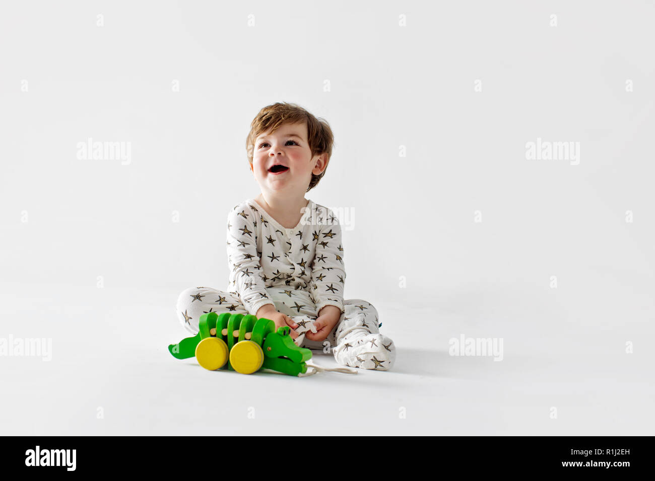 Portrait of smiling toddler boy sitting on floor with toy crocodile. Banque D'Images