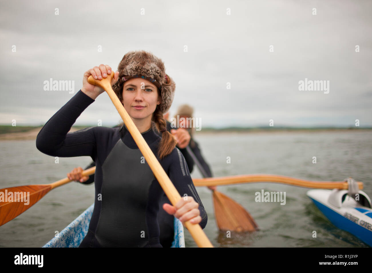Portrait d'une jeune femme portant un chapeau de fourrure et wetsuit tout en pagayant en canoë avec des amis. Banque D'Images