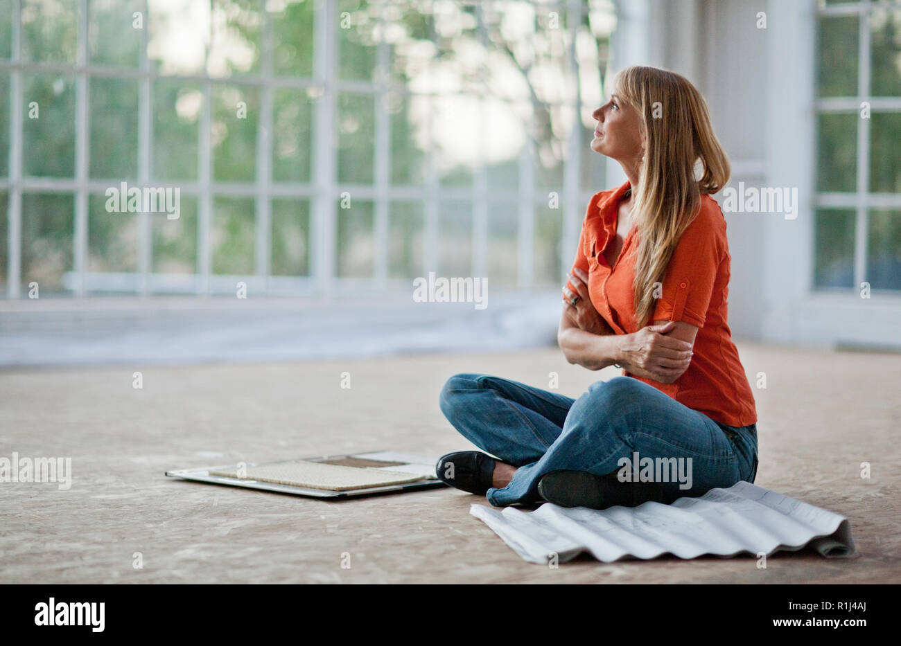 Mid adult woman assis en tailleur sur le plancher avec ses bras croisés. Banque D'Images