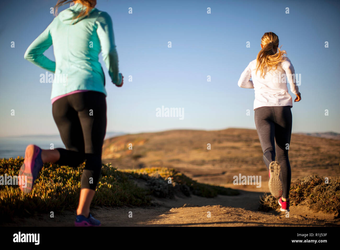 Deux jeunes femmes vont pour un lever ensemble jogging le long de la falaise, à l'océan. Banque D'Images