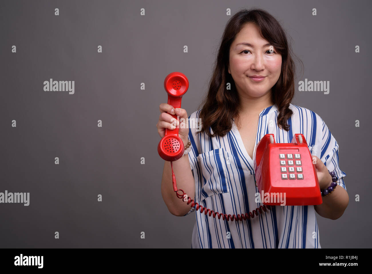 Belle asiatique mature businesswoman holding old red phone Banque D'Images