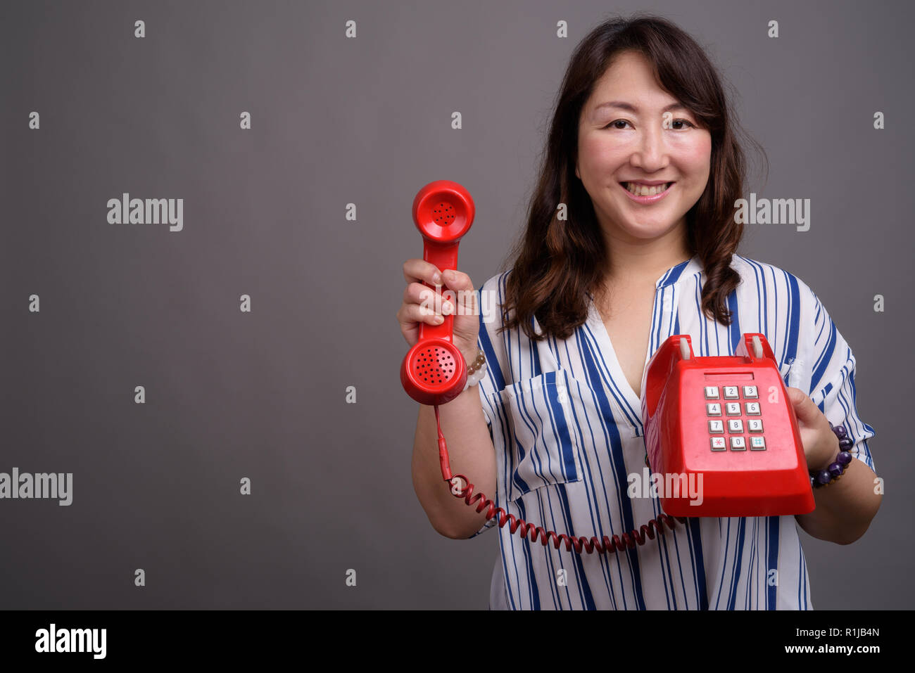 Belle asiatique mature businesswoman holding old red phone Banque D'Images