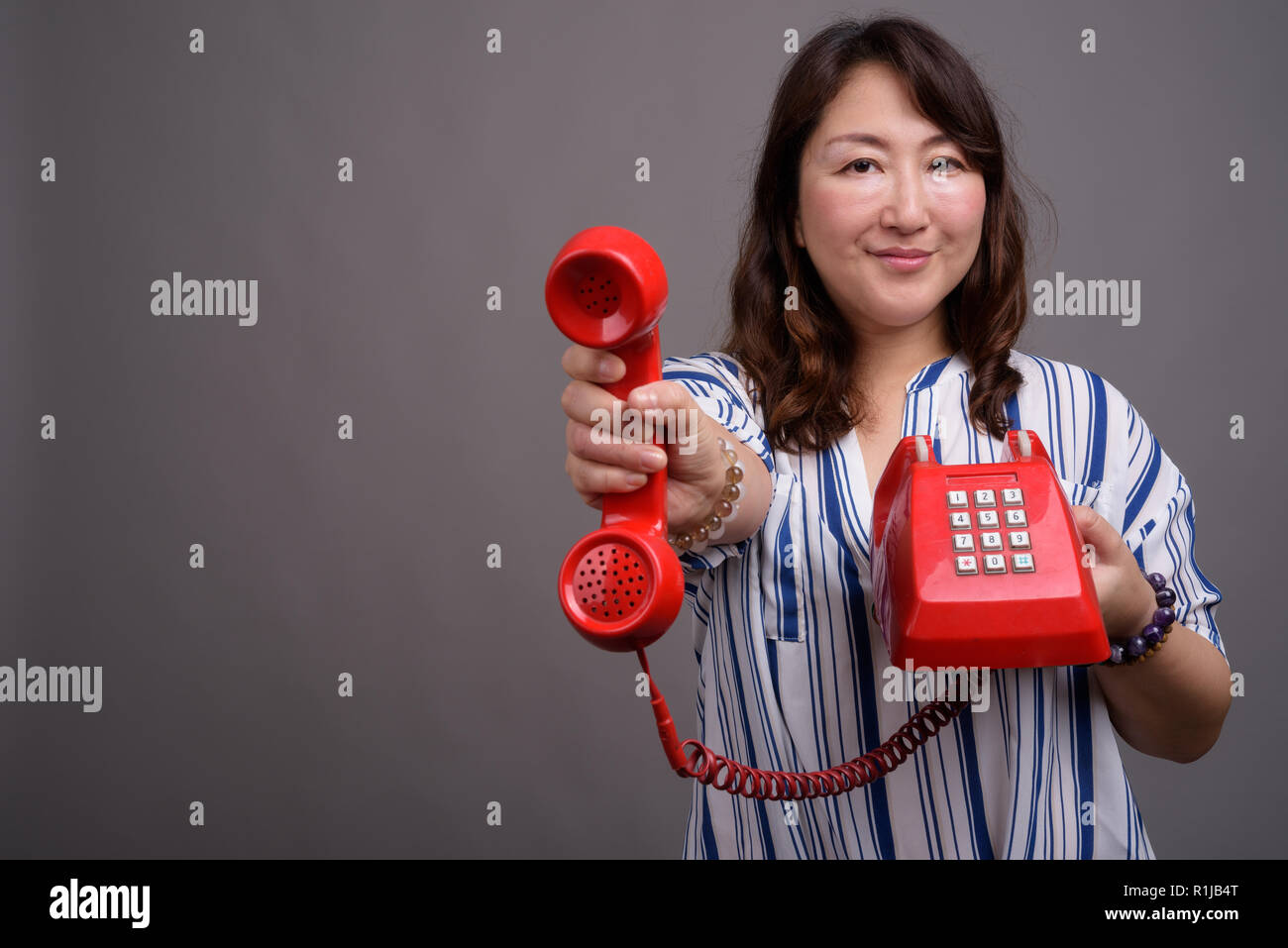Belle asiatique mature businesswoman holding old red phone Banque D'Images