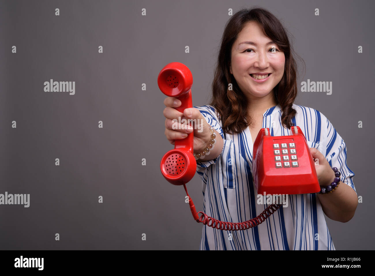 Belle asiatique mature businesswoman holding old red phone Banque D'Images