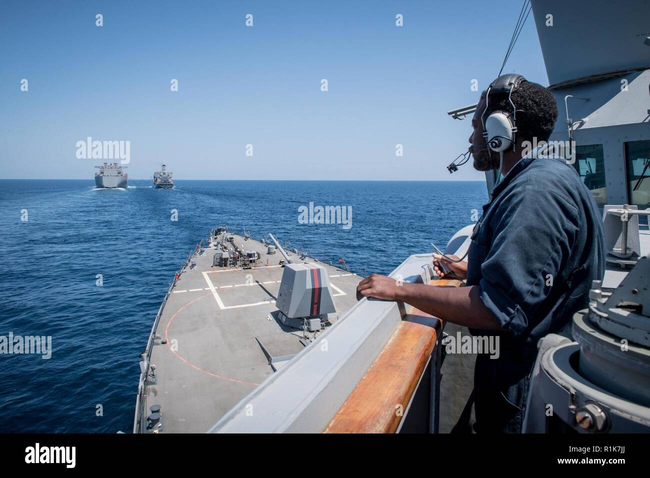 U.S. 5ÈME ZONE DES OPÉRATIONS DE LA FLOTTE (oct. 9, 2018) Spécialiste culinaire Seaman Reginald Smith s'watch sur l'aileron de passerelle de l'USS destroyer lance-missiles Jason Dunham (DDG 109) comme la plate-forme de base mobile expéditionnaire USS Lewis B. Extracteur (ESB 3), à gauche, et la reconstitution de la flotte oiler USNS Henry J. Kaiser (T-AO 187) conduite d'un ravitaillement en mer. Dunham est déployé sur le 5e flotte américaine zone d'opérations à l'appui des opérations navales pour assurer la stabilité et la sécurité maritime dans la région Centrale, reliant la Méditerranée et le Pacifique à travers l'O Banque D'Images