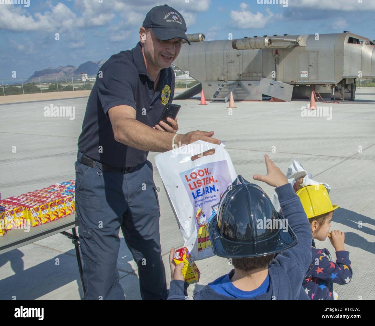 La base navale américaine de la baie de Souda, Grèce (oct. 9, 2018) Vasilis Aggelaskis , un pompier affecté à la base navale américaine (NSA) Baie de Souda, Grèce, passe hors sacs cadeaux pour les élèves de l'école privée Mavromataki durant la Semaine de la prévention des incendies à bord de l'installation le 9 octobre 2018. La NSA Souda Bay Fire & Emergency Services Department a fait équipe avec la National Fire Protection Association (NFPA) pour promouvoir cette année, la campagne de la Semaine de prévention des incendies, "l'aspect. Écouter. En savoir. Être au courant. Le feu peut se produire n'importe où, qui s'efforce de sensibiliser le public au sujet des moyens de base mais essentielles Banque D'Images