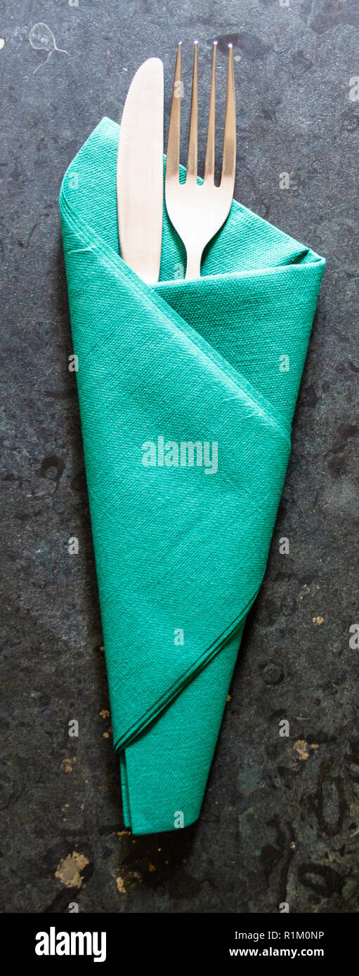 Fourchette et couteau enveloppé dans une serviette de papier vert sur une surface en marbre ou granit sombre Banque D'Images