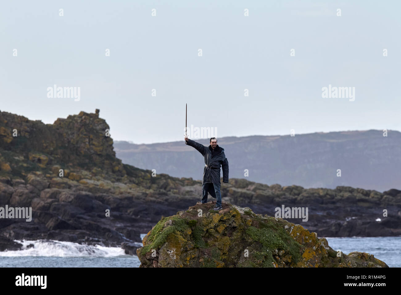 L'homme portant costume tenant un sabre en altitude debout sur des rochers sur un jeu des trônes coach tour guidé à Ballintoy sur le Nord de l'Ireland north coas Banque D'Images