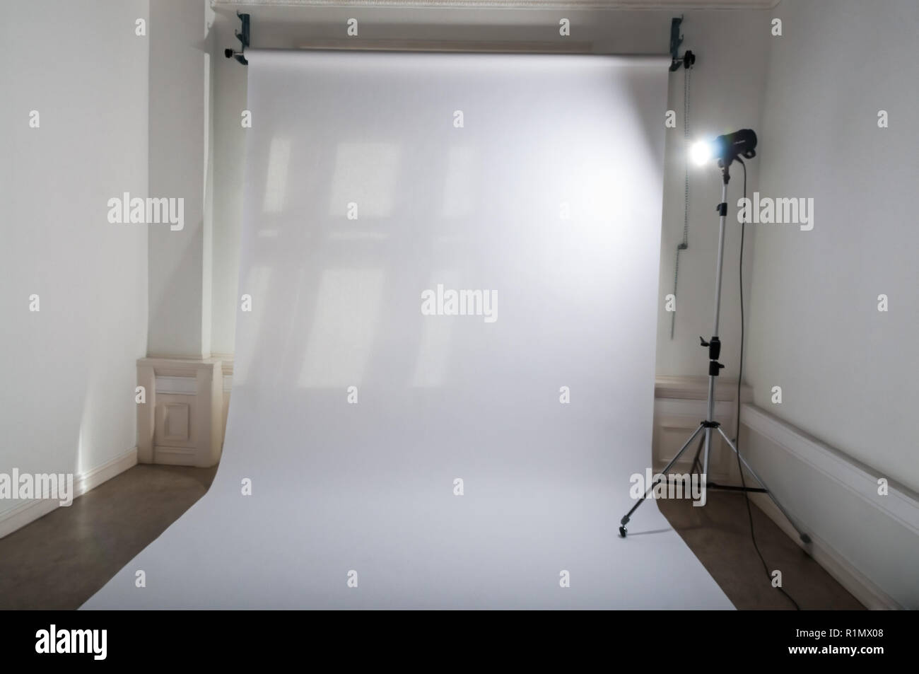 Un studio photo professionnel vide avec propre et simple de configuration de l'équipement photographique, papier ordinaire blanc en toile de fond et un flash lumineux d'une lampe de projecteur sur trépied dans un atelier en grisé Banque D'Images