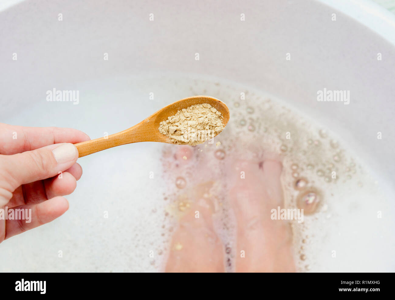 Femme prenant un bain de pieds réchauffement de guérison avec de la moutarde en poudre, l'ajout de moutarde en poudre pour bain de pied avec une cuillère de bois. Contre le froid la maladie, les maux et les im Banque D'Images