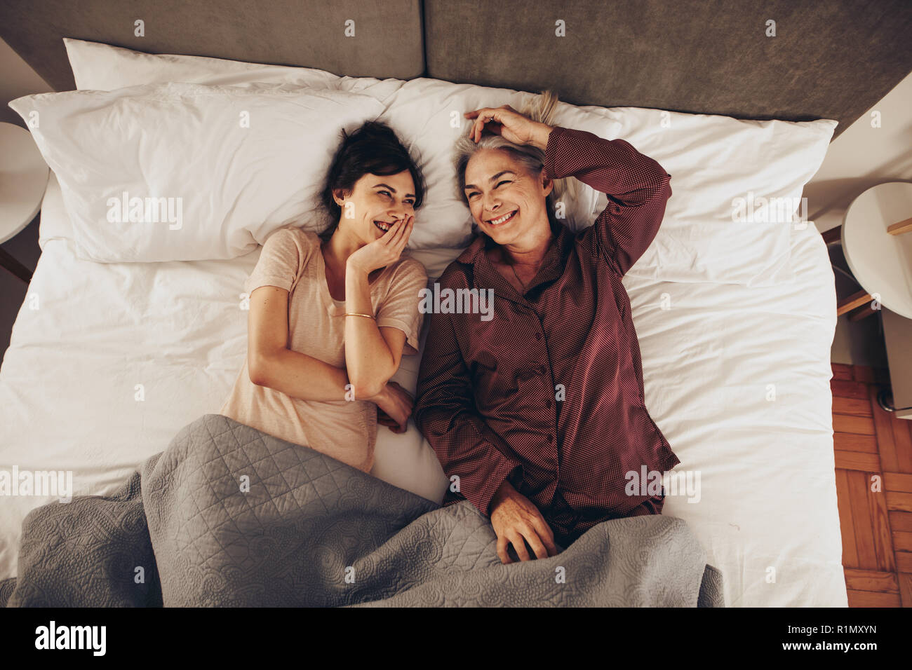 Top View of smiling mother and daughter lying on bed at home. Dormir à côté de sa mère, femme et rire avec la main sur la bouche. Banque D'Images