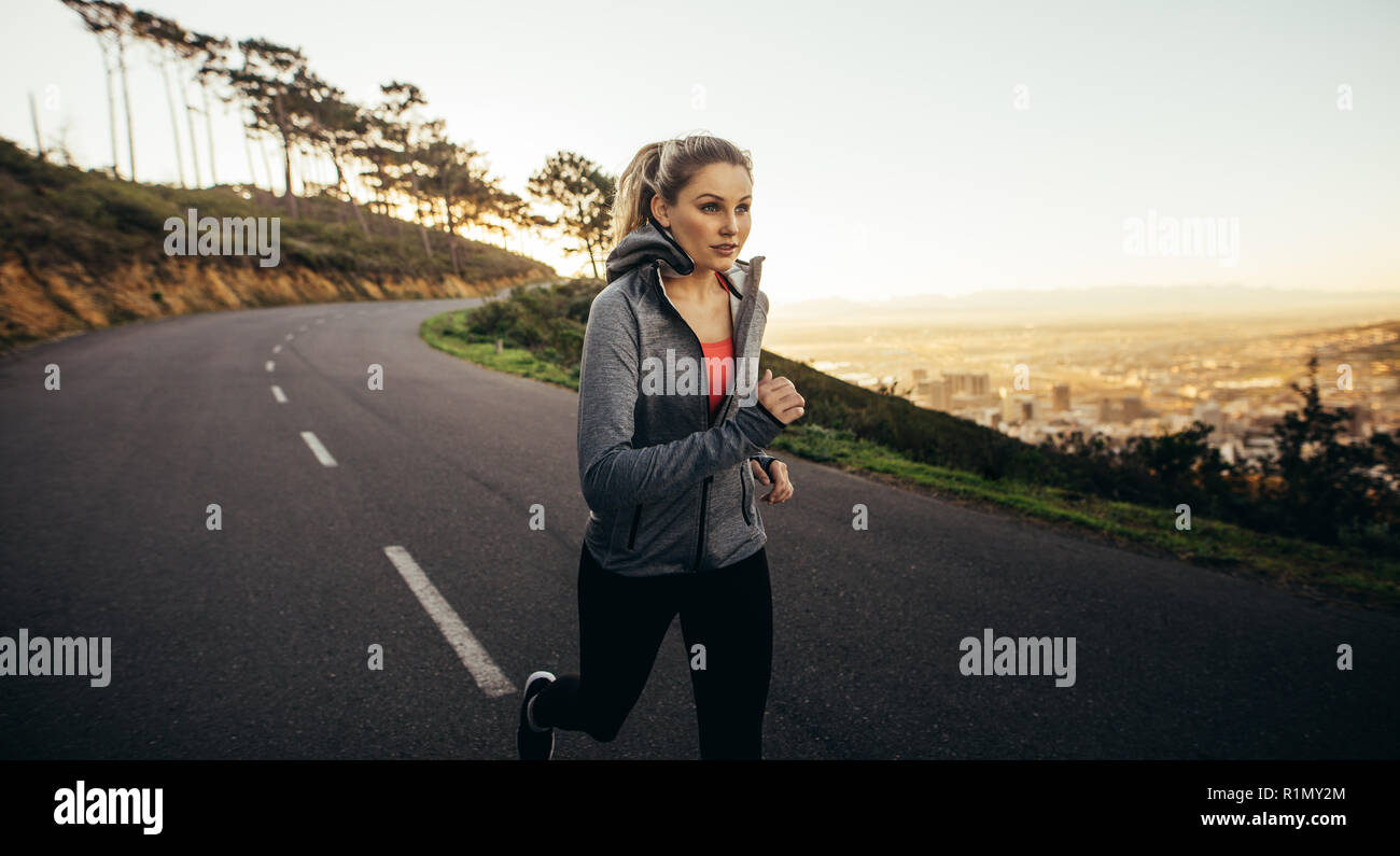 Femme en vêtements de fitness courant dans une rue vide le matin. femme de fitness jogging sur une route vallonnée. Banque D'Images
