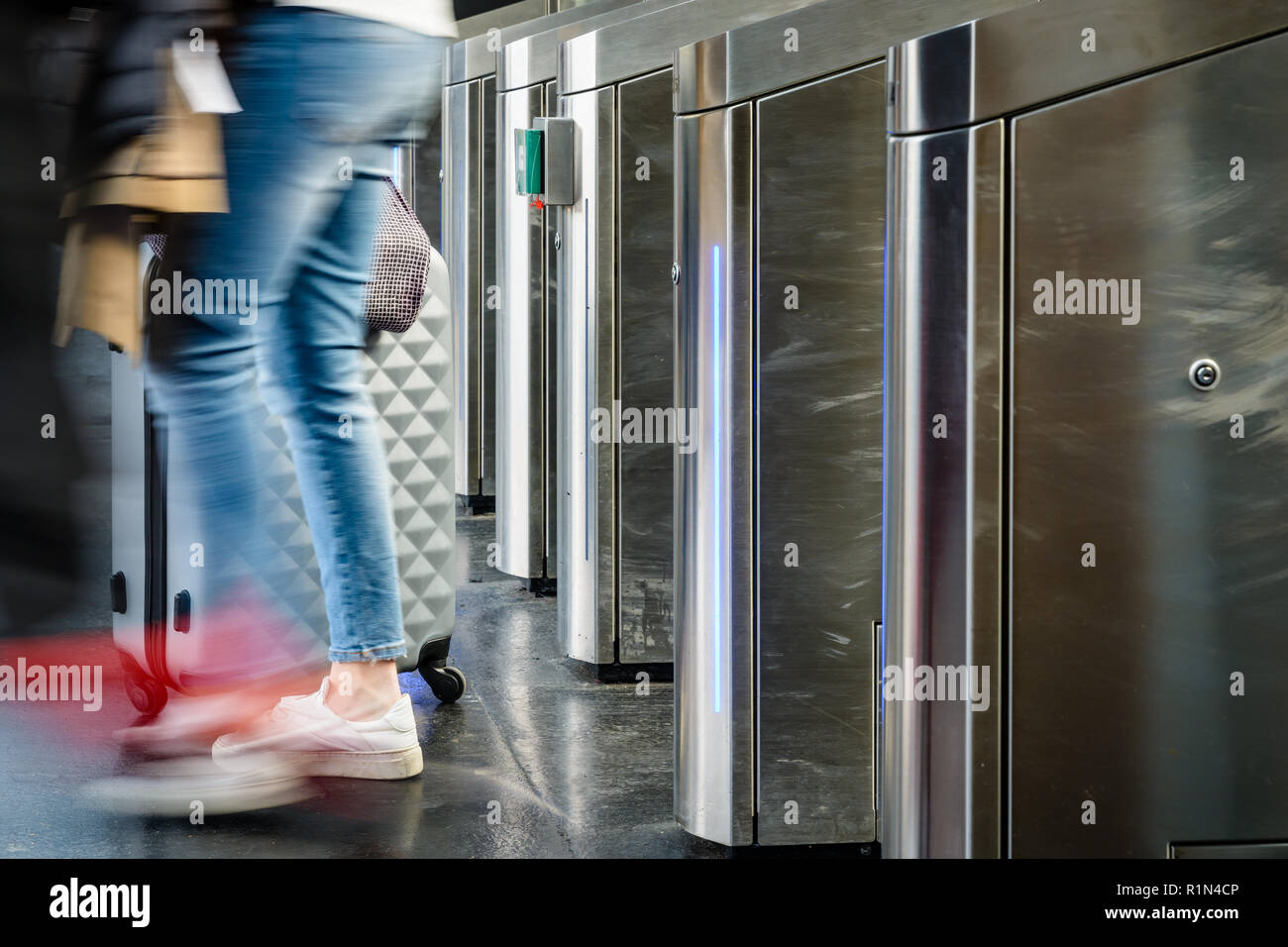 Vue latérale d'une femme avec une valise roulant en passant par des portes en acier inoxydable d'un ticket de transport public station in Paris with motion blur Banque D'Images