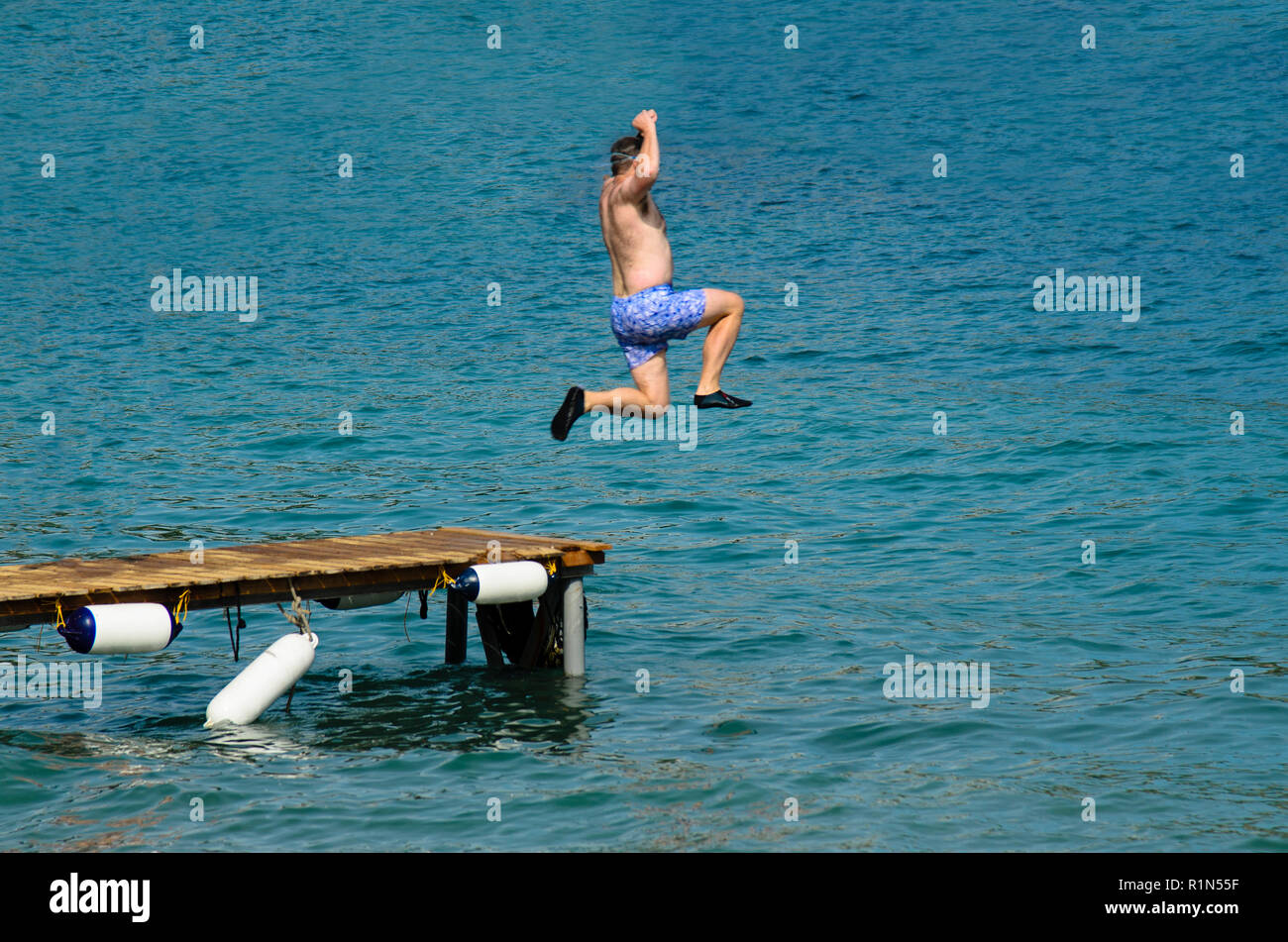 L'homme en maillot de sauter dans la mer depuis une jetée en bois, portant des chaussures en caoutchouc noir Banque D'Images