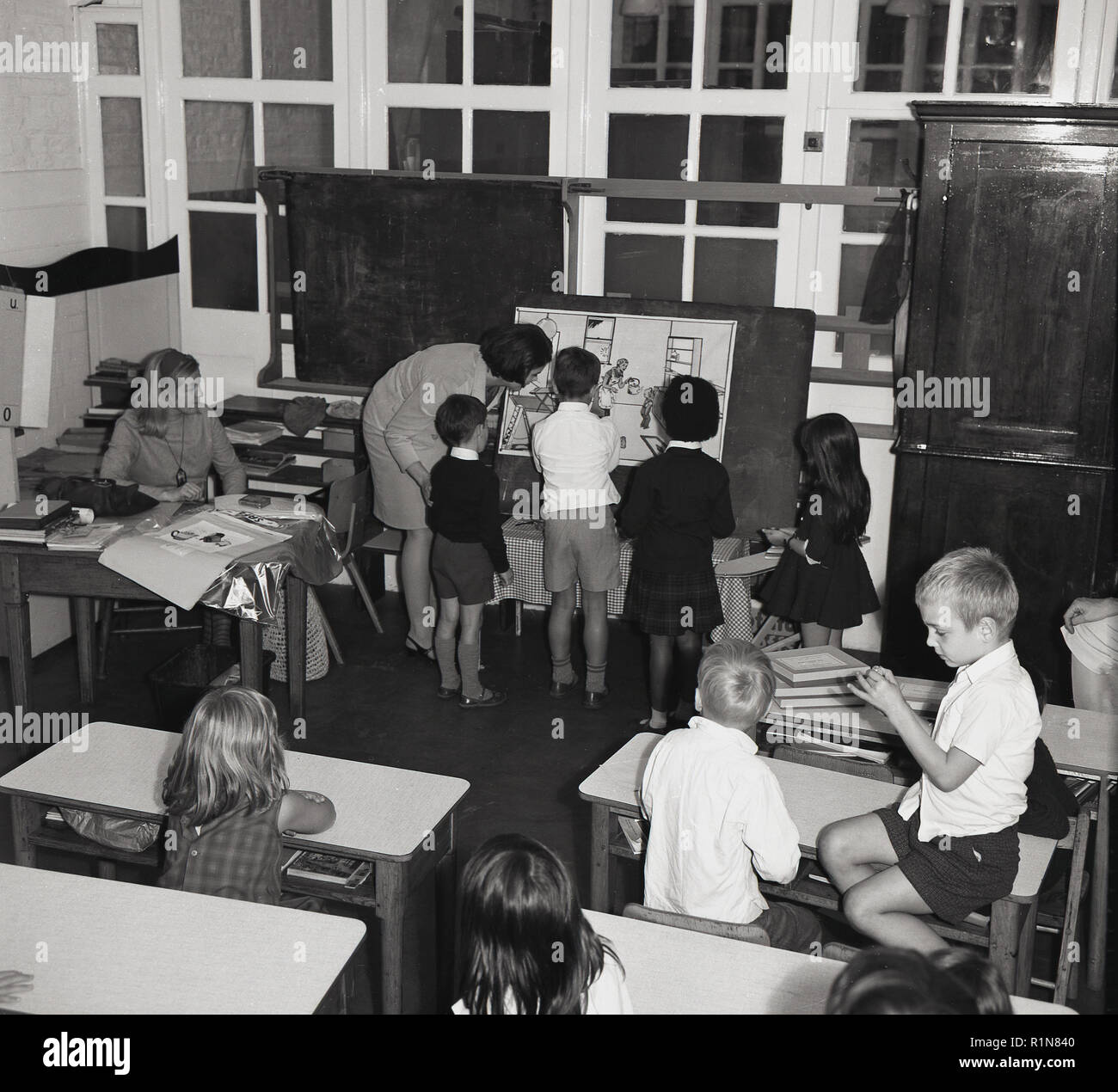 Années 1950, les jeunes enfants avec l'enseignant à l'intérieur d'une pépinière ou jouer-école, en Grande-Bretagne d'après-guerre. Intéressant de voir comment il a été formel, puis une salle de classe avec un bureau approprié mis côte à côte et même un tableau noir. Banque D'Images