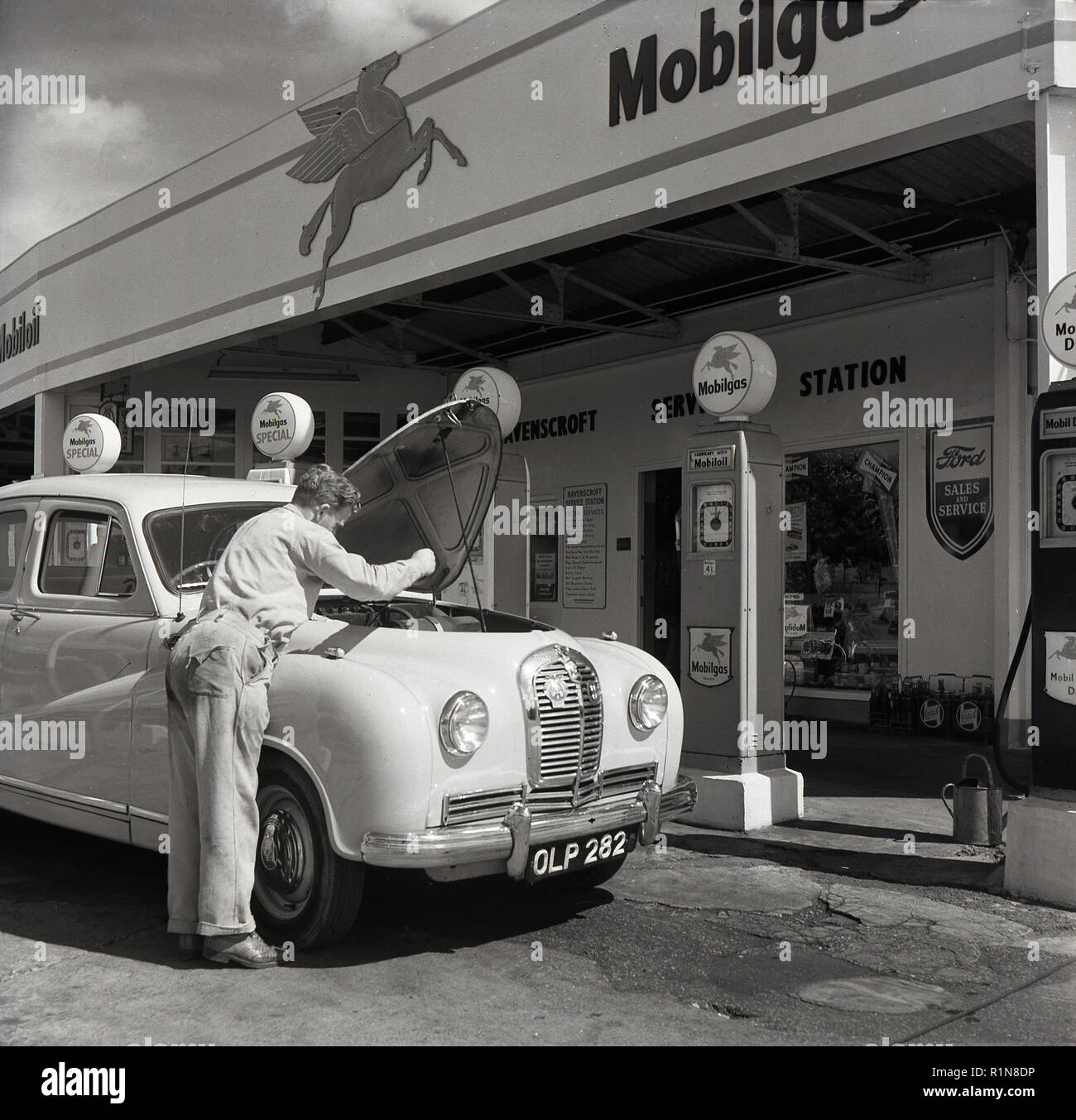 Années 1950, historiques, l'âge d'or de l'automobile, une station service sttendant vérifie l'huile sur une voiture garée à Austin les pompes à essence à la Station Service Mobilgas Ravenscroft, Great West Road, London, England, UK. Banque D'Images