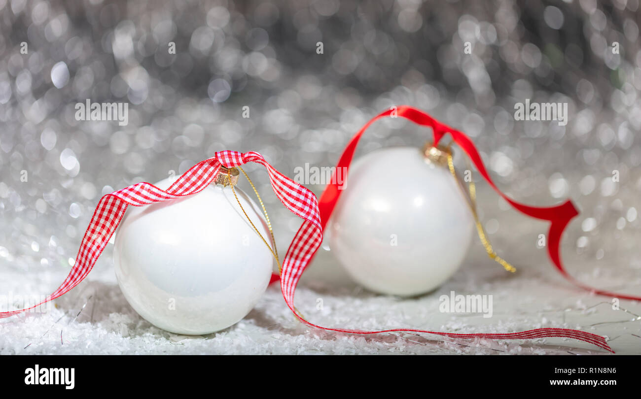 Boules blanches de Noël, ruban rouge et neige, lumières fond flou abstrait Banque D'Images