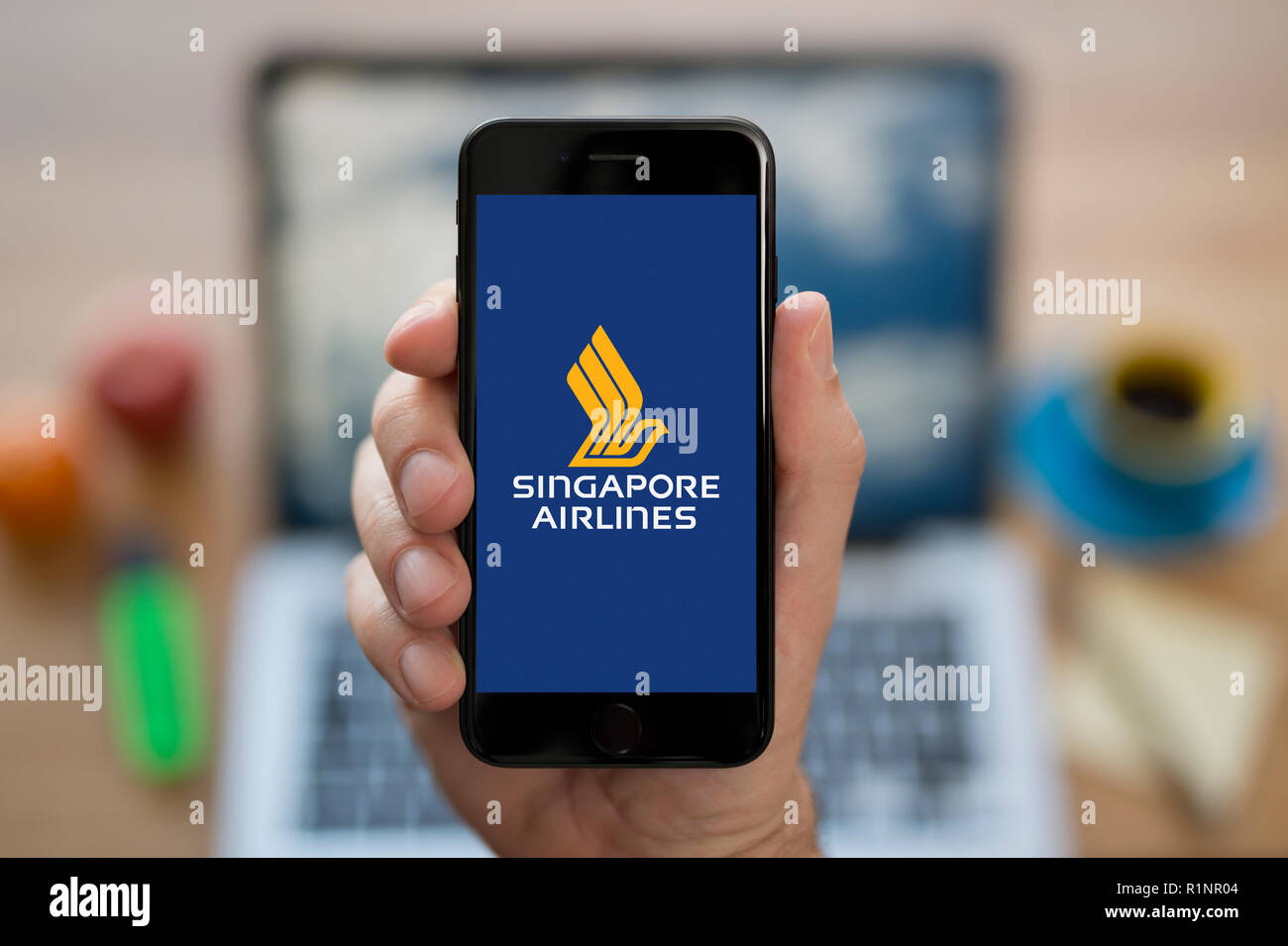 Un homme se penche sur son iPhone qui affiche le logo de Singapore Airlines, en restant assis devant son ordinateur 24 (usage éditorial uniquement). Banque D'Images