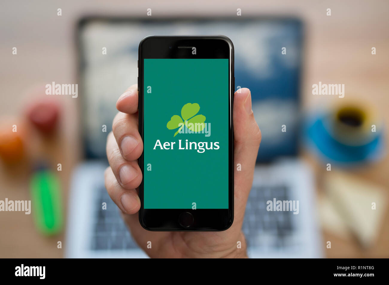 Un homme se penche sur son iPhone qui affiche le logo d'Aer Lingus, tandis qu'assis à son bureau de l'ordinateur (usage éditorial uniquement). Banque D'Images